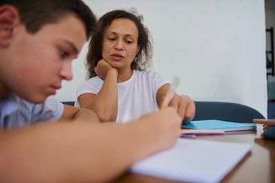 A woman attentively helps a young boy with his homework.