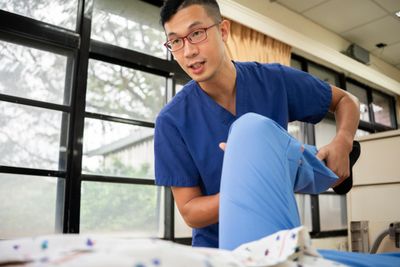 Physical therapist assisting a patient with leg exercises in a clinical setting.
