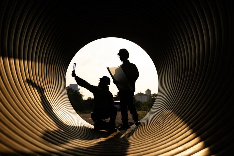 Construction workers and engineers are working efficiently inside a large metal pipe at a construction site. They are building a new water drainage system in the evening, just before sunset.
