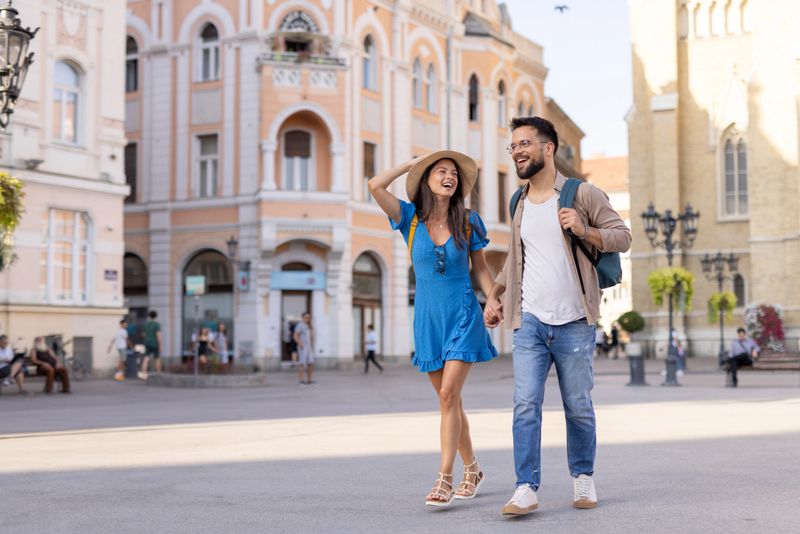 A happy couple walks hand-in-hand in a sunny city square, with historic architecture in the background, embodying joy, love, and the beauty of travel together.