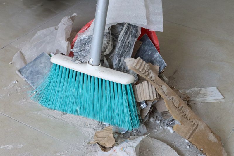 Stock photo showing close-up view of a short-handled broom with a heap of rubbish, dust and dirt swept up on a tiled floor.