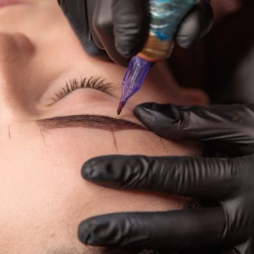 Close-up of eyebrow tattooing with a needle and black gloves.