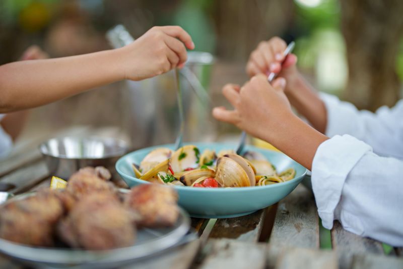 The table is adorned with plates of pasta, featuring seafood ingredients like shrimp and clam, garnished with herbs and spices, likely giving the dish a Mediterranean or Italian flair.