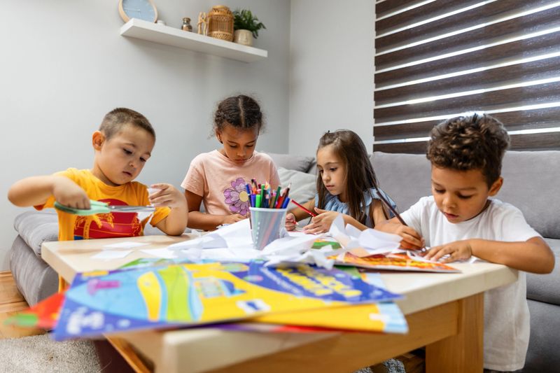 Four children are gathered around a table, engaging in creative activities with paper and colored pencils, fostering collaboration and imagination.
