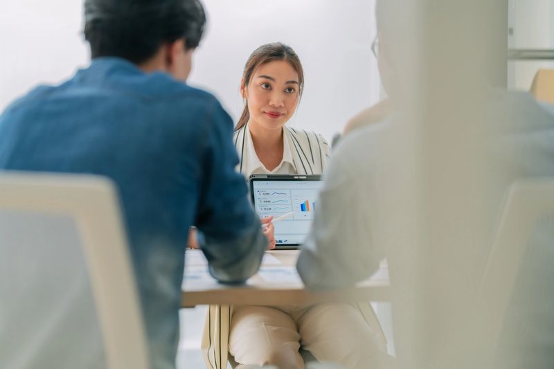 A focused business meeting featuring woman engaged in discussion while reviewing data on laptop. atmosphere is professional and collaborative, highlighting teamwork and communication.