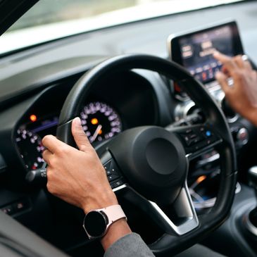 Person using a touchscreen interface inside a car while holding the steering wheel.