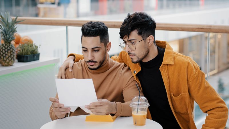 Two friends students sitting in cafe young worried man receiving letter reading bad news upset feels sad failing exam dismissal financial problem loss arab guy comforting best friend hugging cheers up. High quality 4k footage