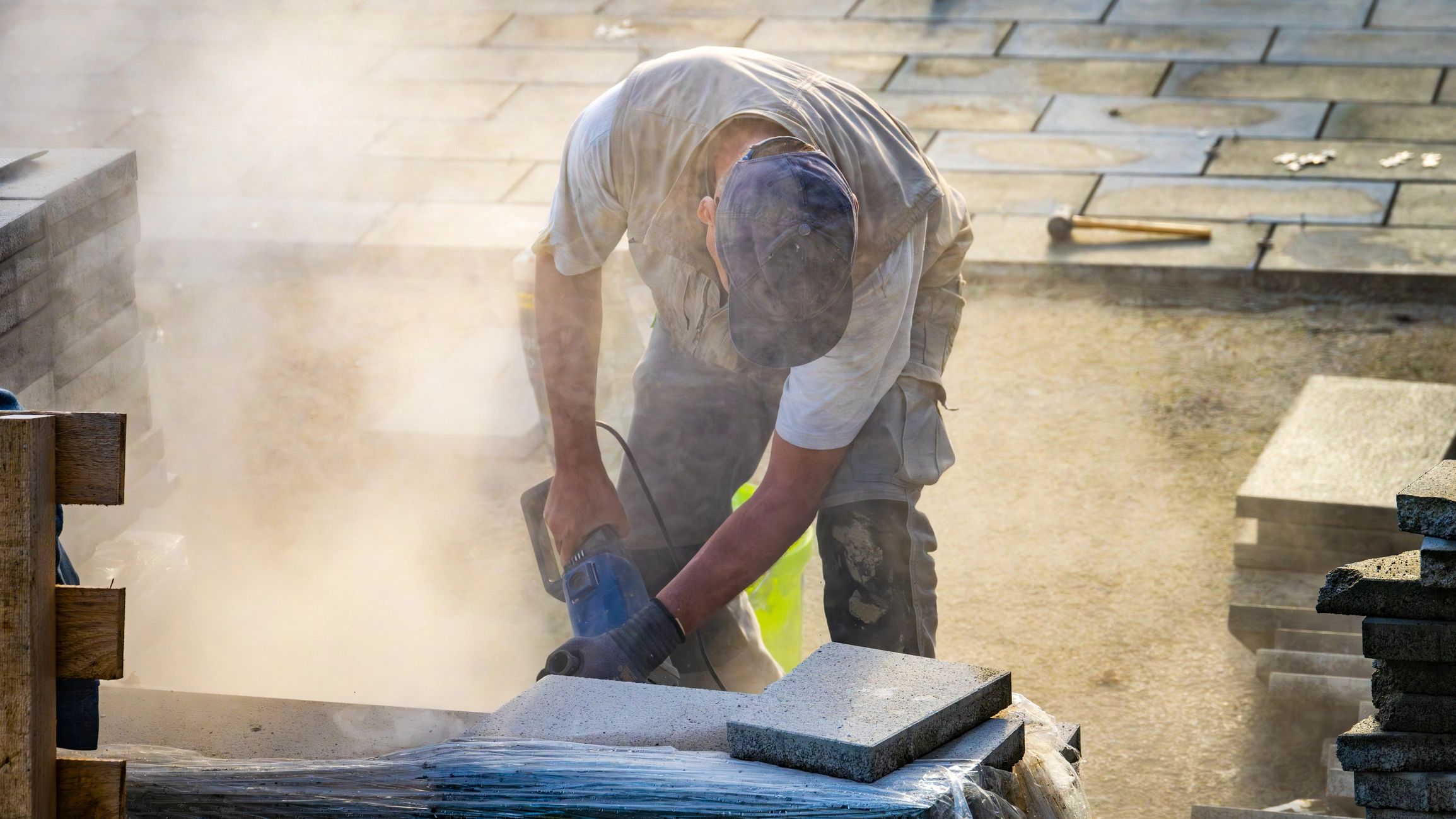 Construction worker cutting stone with a power saw, raising a cloud of dust