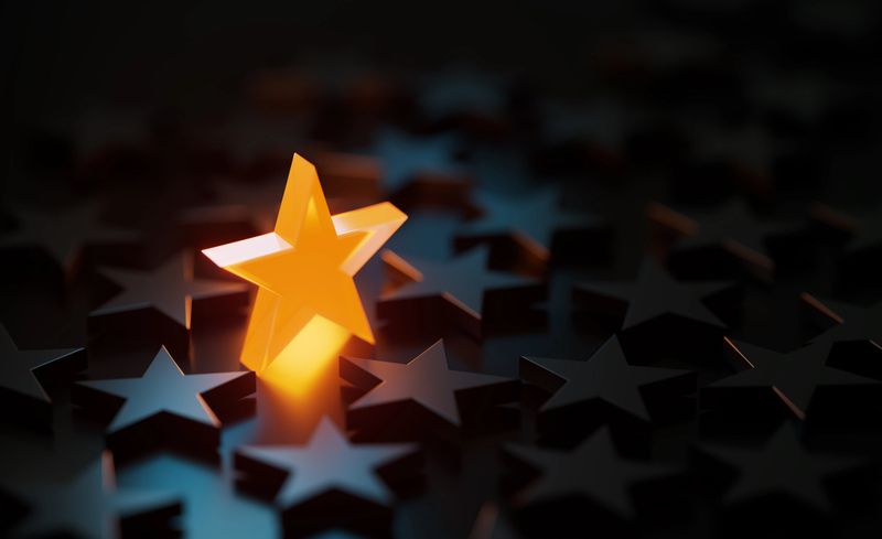 Orange star symbol glowing amid black star symbols on black background. Horizontal composition with copy space.