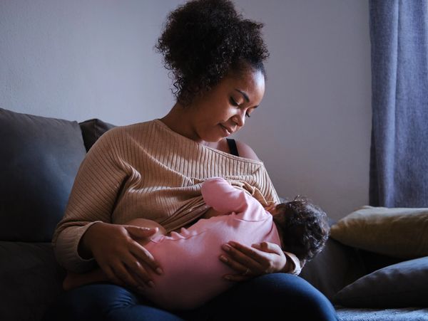 A mother breastfeeding her baby while sitting on a couch.