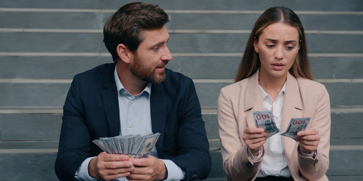 Two businesspeople counting money on stairs, woman looking worried.
