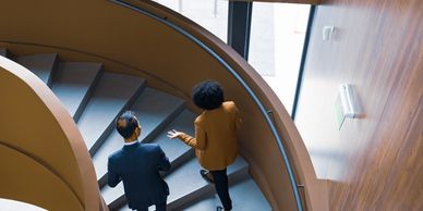 Two colleagues talking while walking down a spiral staircase in an office.