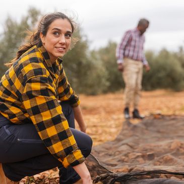 Woman in plaid shirt kneeling and holding a net, man in background in an outdoor setting.