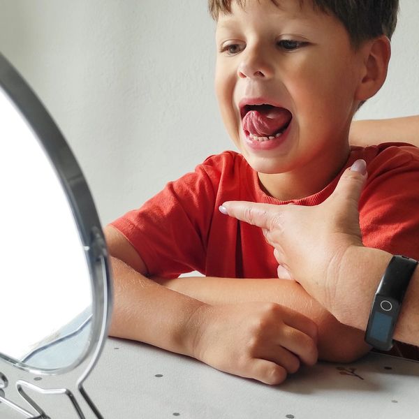 Child practicing tongue movements with guidance in front of a mirror.