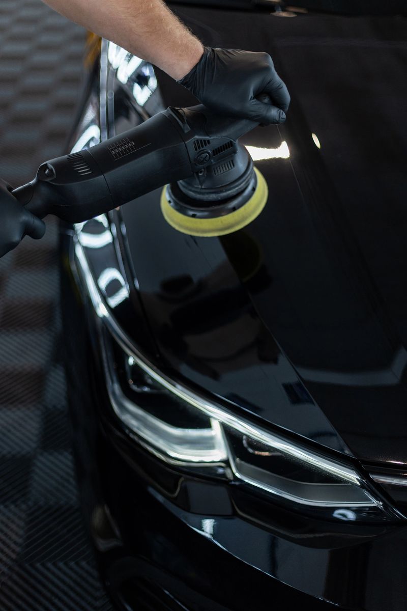 Professional man with polishing tool polishing black car in garage . Detailing. Varnish care and scratch removal