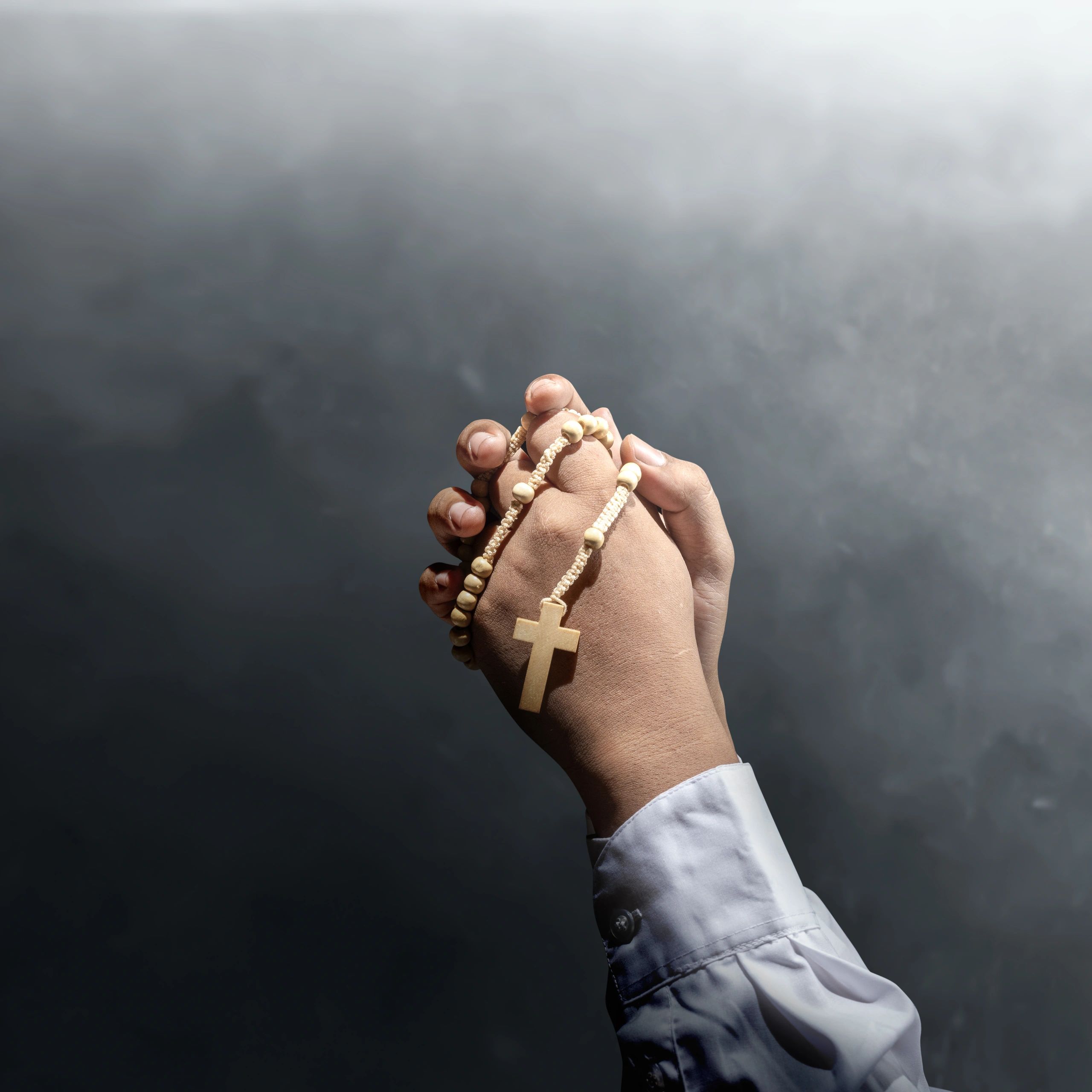 Hands clasped in prayer holding a wooden rosary with a cross.