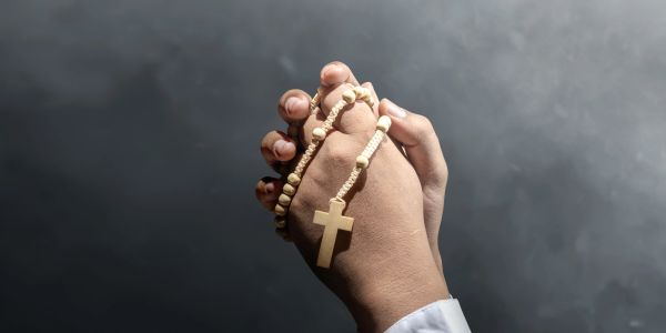 Hands holding a wooden rosary with a cross.