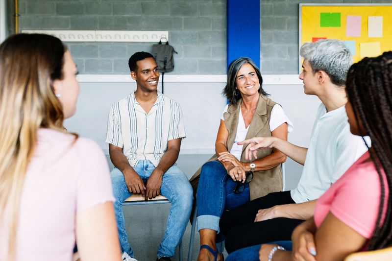 Young group of teenage students discussing in classroom sitting in circle with female teacher, giving an opinion on a debate topic. Education concept