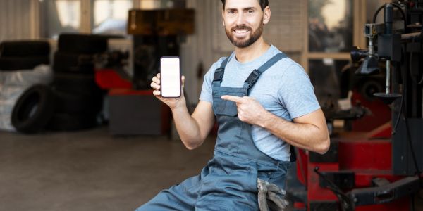 Mechanic showing a smartphone with a blank screen in a workshop.