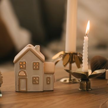 Cozy ceramic house and lit candle on wooden table.
