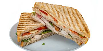 Grilled chicken sandwich with lettuce, tomato, and cheese on a white plate.