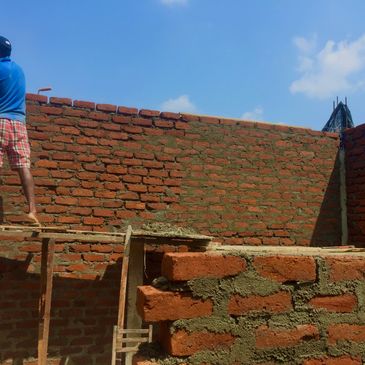 A man building a brick wall under a clear blue sky.