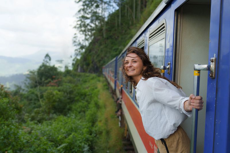 Cheerful woman looking out of train door traveling in Sri Lanka