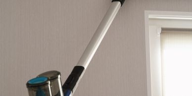 Person using a vacuum cleaner to clean the top of a curtain valance.