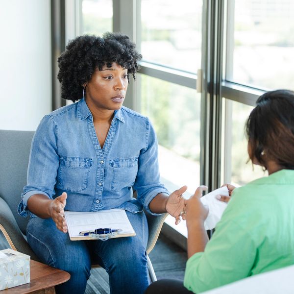 A woman in denim talks seriously with another woman in a counseling session.