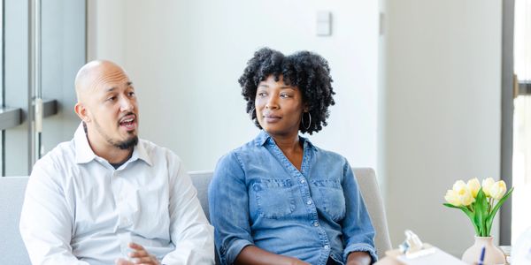 Couple having a serious conversation on a couch in a bright room.