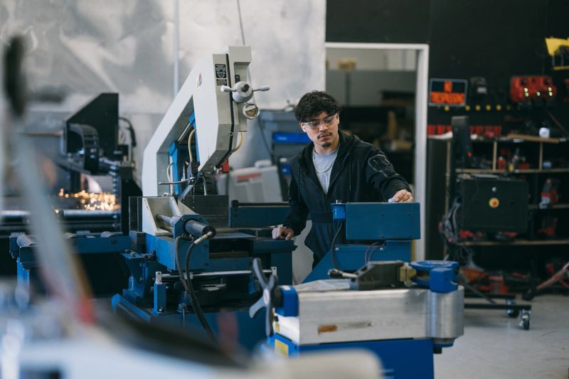 A man operates a CNC machine which engraves metal while working in a manufacturing and fabrication facility.