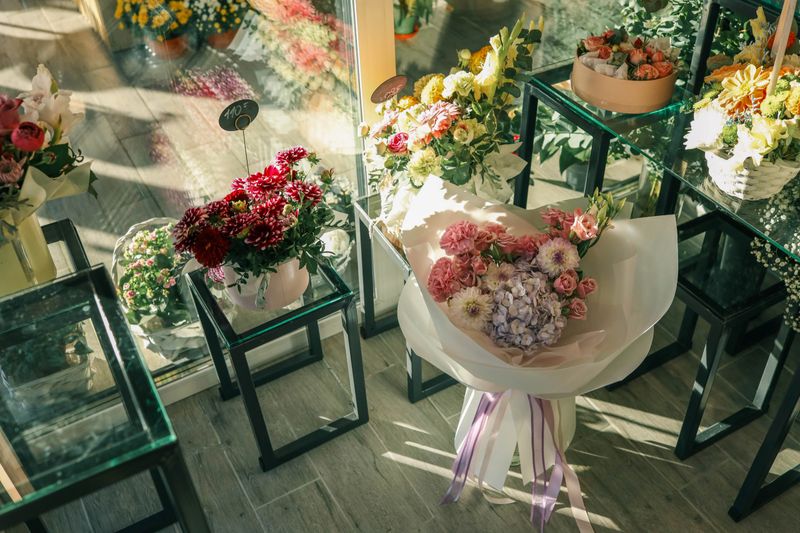 Close-up of vibrant floral bouquets on display, featuring fresh chrysanthemums, roses, and assorted seasonal flowers arranged in paper wraps and baskets under soft sunlight.