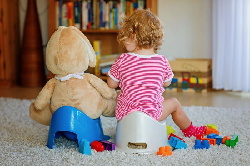 Closeup of cute little 12 months old toddler baby girl child sitting on potty. Kid playing with doll toy. Toilet training concept. Baby learning, development steps.