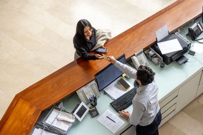 Receptionist handing a card to a smiling woman at the front desk.