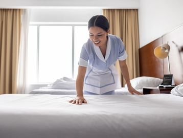 Housekeeper making a hotel bed with a smile.