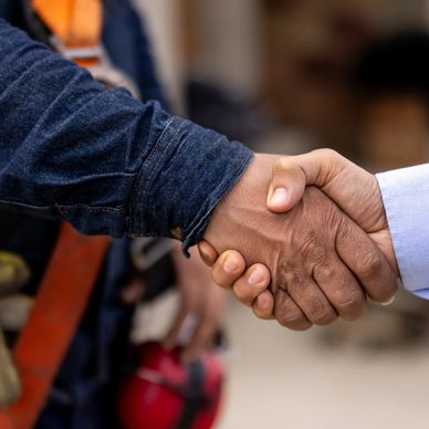 Two people shaking hands, one in workwear and the other in a dress shirt.