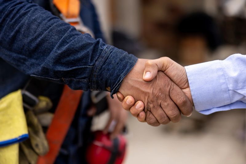 Close-up on a building contractor handshaking with an architect at a construction site
