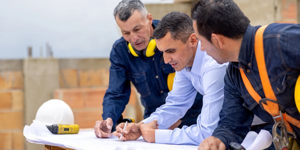 Three men reviewing construction plans on a site with safety gear.