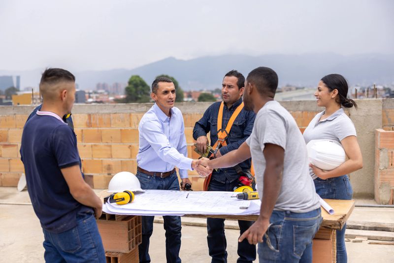 Happy Latin American architect greeting a construction worker with a handshake at a construction site