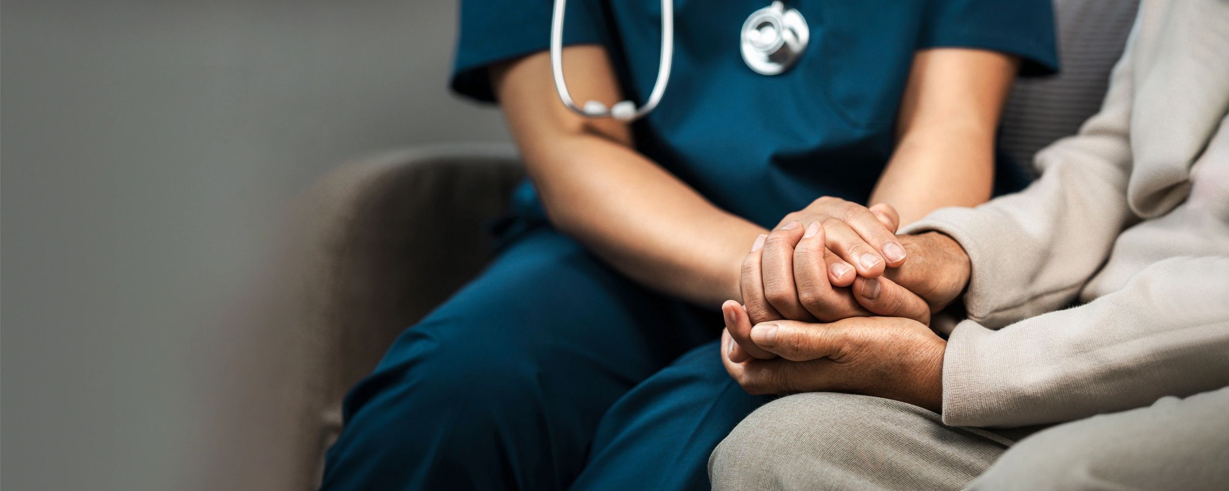 Healthcare worker holding elderly patient's hand in comforting gesture.