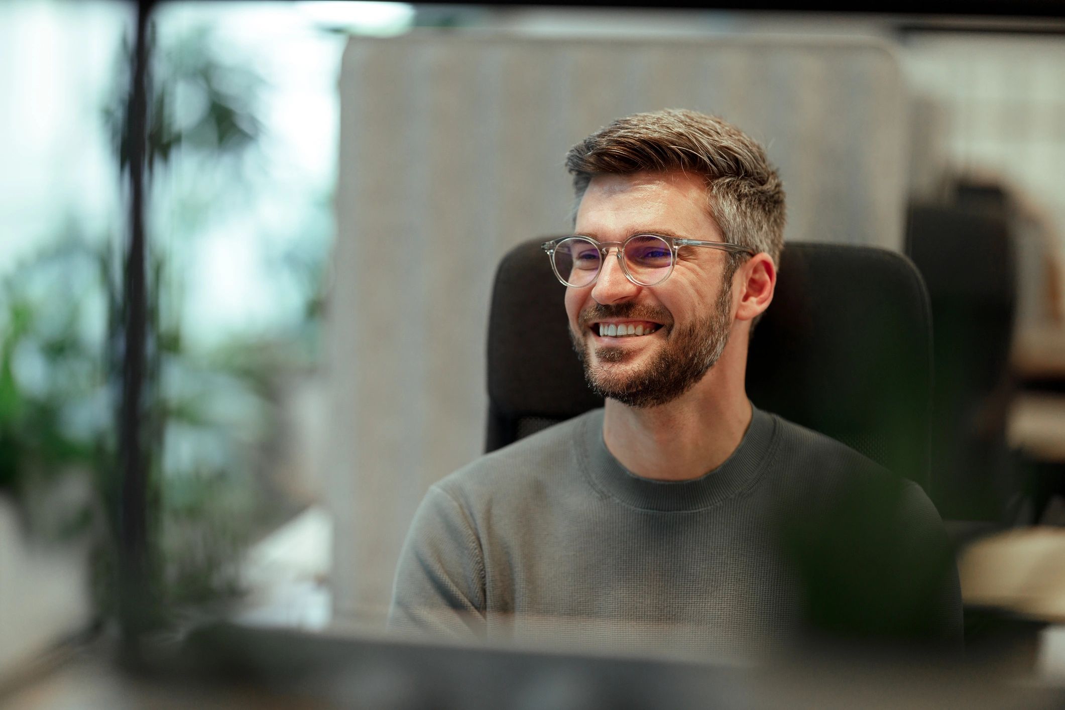Man with beard and glasses sitting in a comfortable office chair, happily smiling