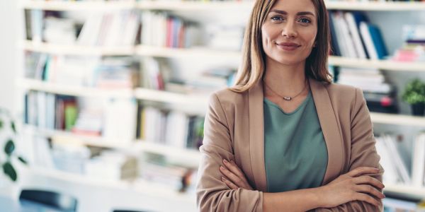 Confident woman standing with arms crossed in a library.
