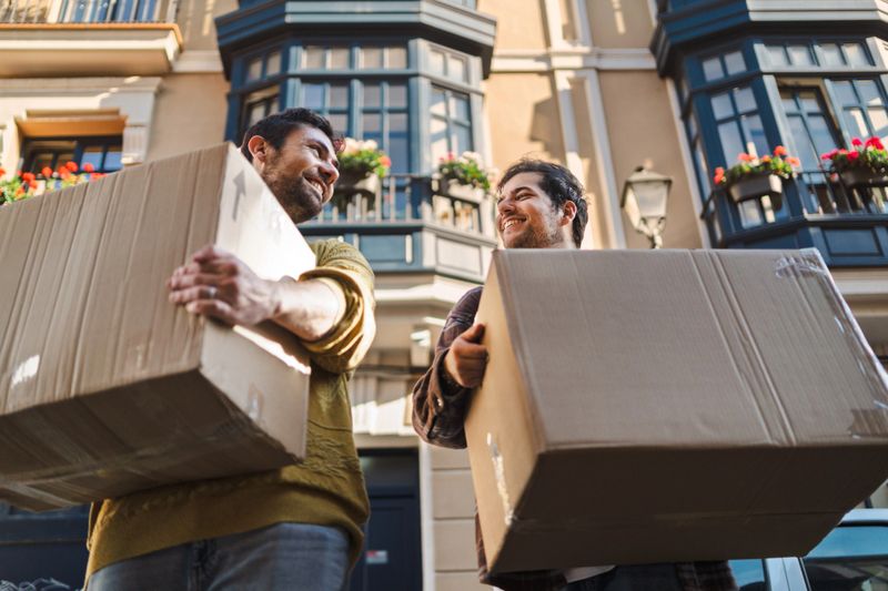 Joyful couple happily moving into a new home, holding cardboard boxes