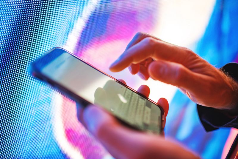 Closeup of mobile in hands with neon light billboard at background