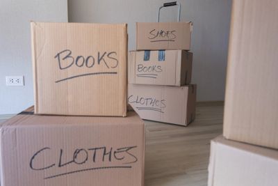 Stacked moving boxes labeled with books, clothes, and shoes in a room. Move in/ Move out cleaning