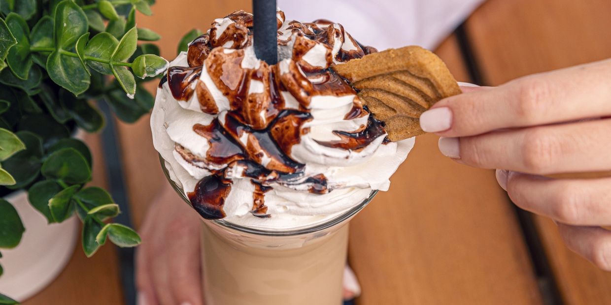 A creamy iced coffee topped with whipped cream, chocolate drizzle, and a cookie.