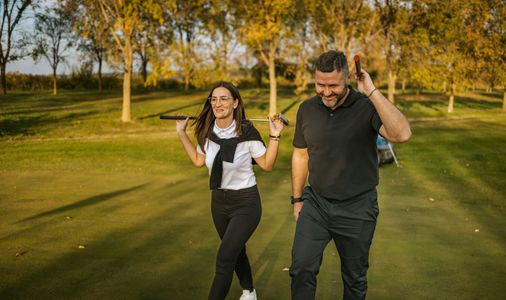 Golf instructor helping player with putting stance on green.
