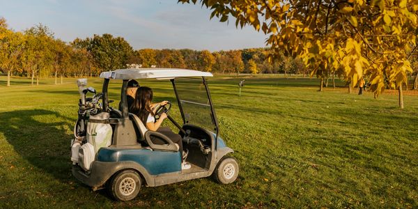 Personas en carrito de golf en campo verde durante otoño.