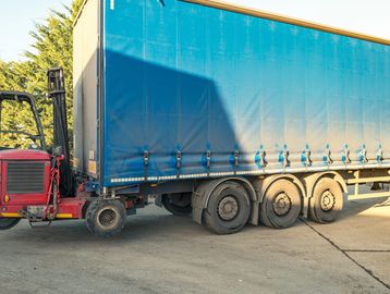 Blue trailer attached to a red forklift on a sunny day.