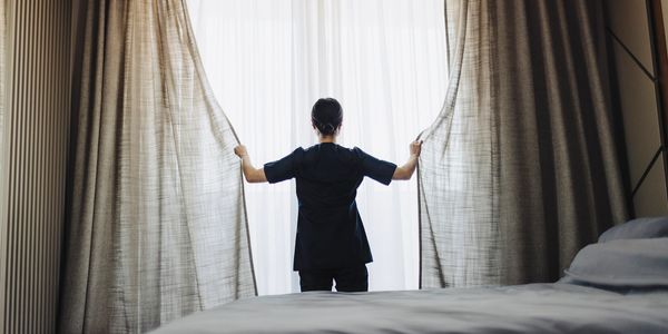 Person opening curtains in a bedroom with soft daylight.
